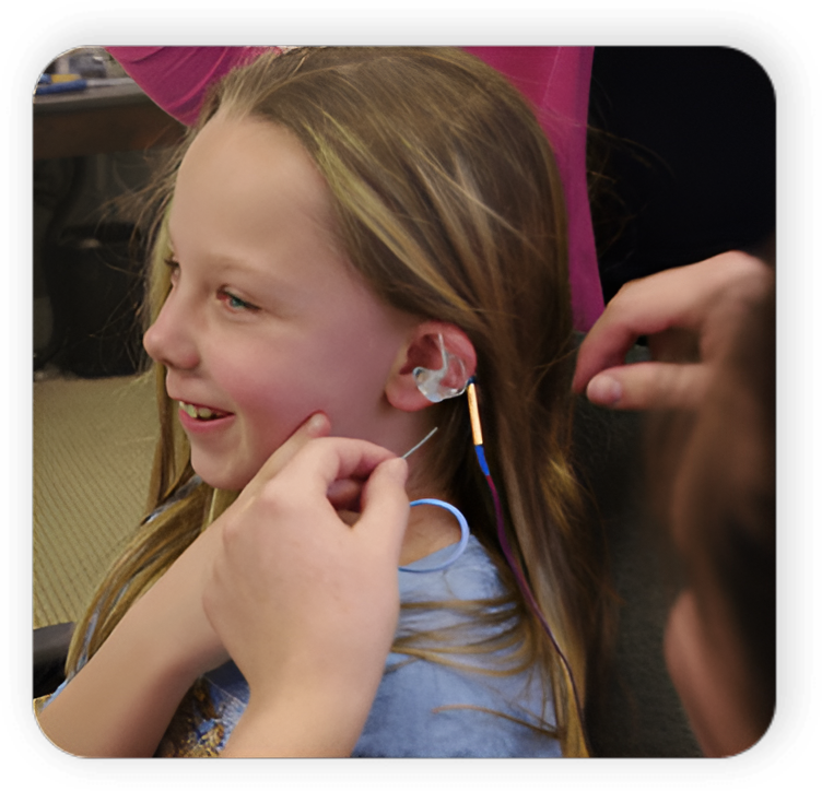 A girl with ear buds is being fitted for an earpiece.